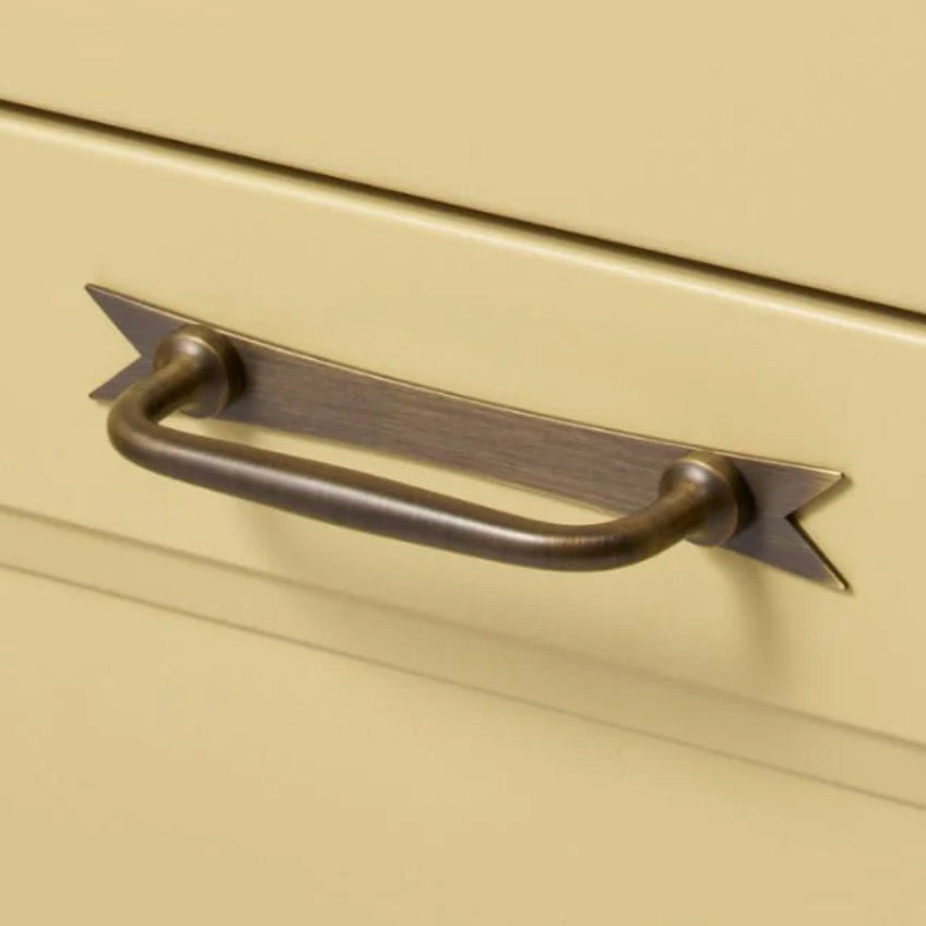 Cabinet Handle in Antique Brass with Ribbon Backplate on a light yellow cabinet. 